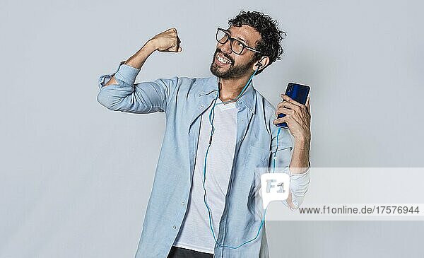 Glücklicher Mann mit Kopfhörern hält ein Handy und feiert  Ein Mann mit seinem Smartphone feiert den Sieg