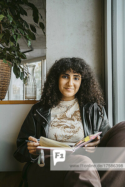 Porträt einer jungen Frau  die mit einem Buch an der Universität sitzt