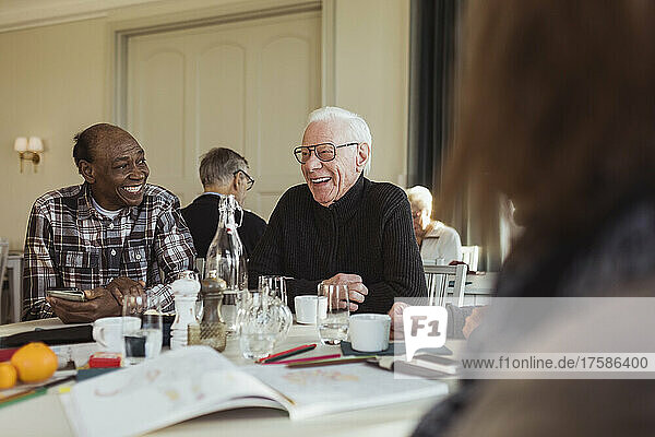 Fröhliche ältere männliche Freunde unterhalten sich am Tisch im Altersheim