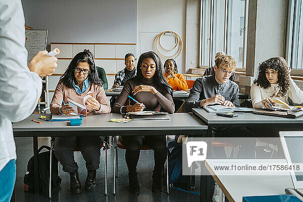 Multirassische Schüler sitzen am Schreibtisch und lernen vom Lehrer im Klassenzimmer