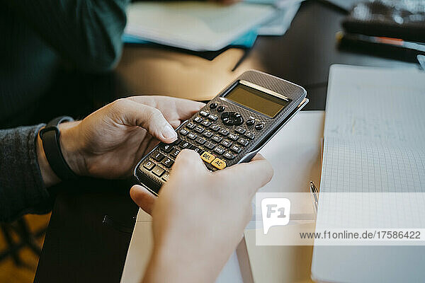 Hands of young male student using calculator at university
