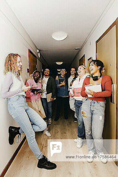 Multiracial students looking at female friend and laughing at corridor in college dorm