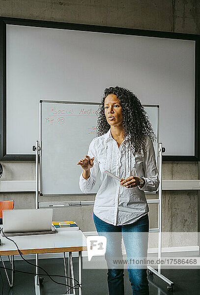 Selbstbewusster Lehrer mit lockigem schwarzem Haar  der vor einer Tafel im Klassenzimmer einer Hochschule erklärt
