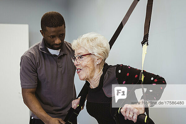 Ältere Frau beim Dehnen eines Widerstandsbands durch einen männlichen Pfleger im Altersheim