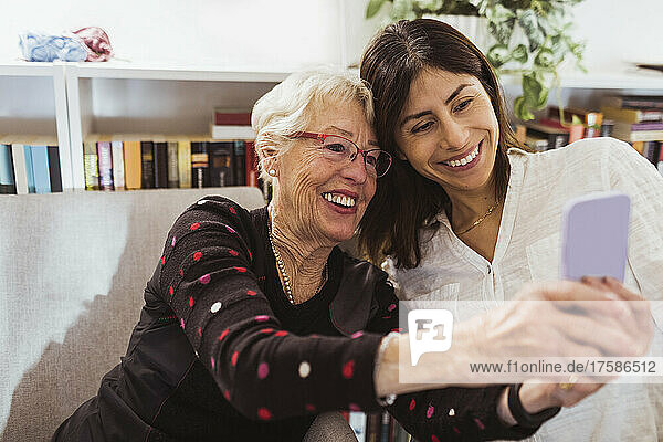 Smiling senior woman taking selfie with female caregiver in nursing home