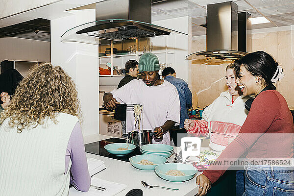 Multiracial young man and women with male friend serving noodles in college dorm