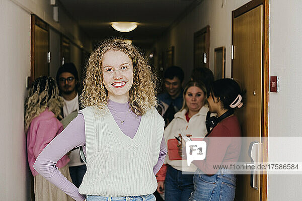 Portrait of smiling young woman with multiracial friends in background at corridor in college dorm