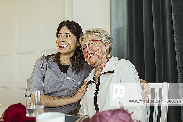 Glückliche Mitarbeiterin im Gesundheitswesen  die mit einer älteren Frau in einem Pflegeheim zusammensitzt