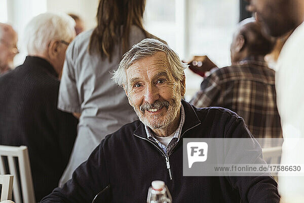 Portrait of smiling senior man with caregiver and friends in background at nursing home