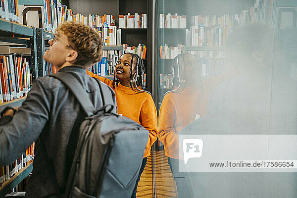 Young friends searching book together in library at university