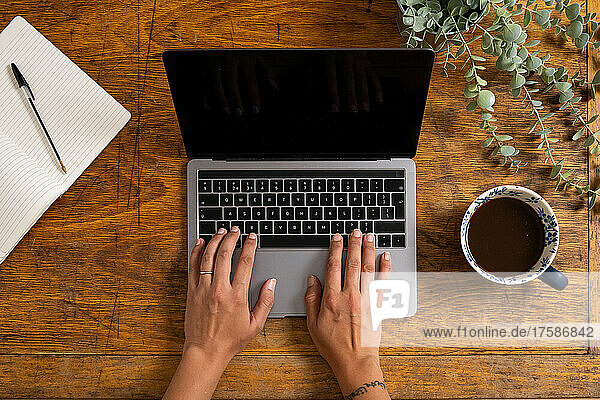 Overhead view of hands of woman typing on laptop on old wooden desk