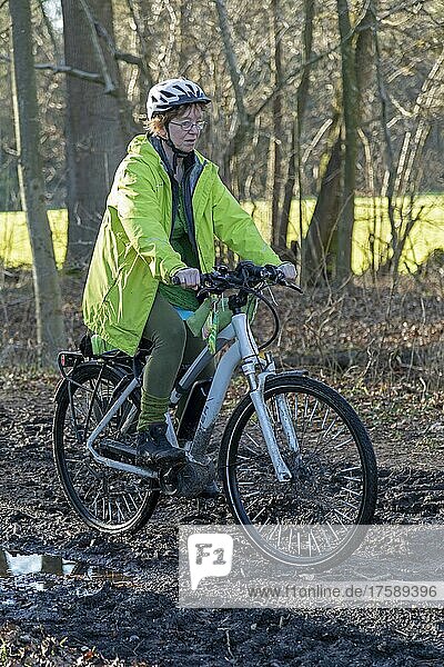 Woman cycling with e-bike over muddy forest path and through puddles  Lüneburg  Lower Saxony  Germany  Europe