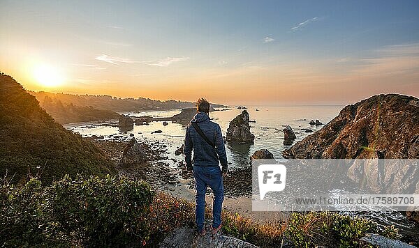 Young man looking at the sea and sandy beach Harris Beach with rocks at sunrise  Harris Beach State Park  Brookings  Oregon  USA  North America