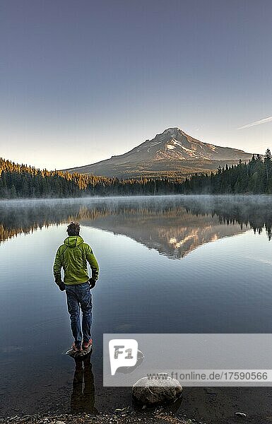 Junger Mann steht auf Stein  Spiegelung des Vulkans Mt. Hood im See Trillium Lake  bei Sonnenaufgang  Oregon  USA  Nordamerika