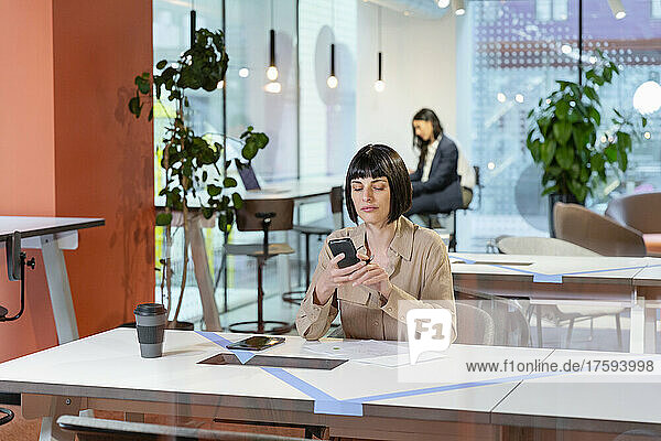 Manager text messaging on smart phone at desk in office