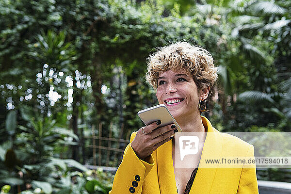 Happy woman talking on speaker phone in park