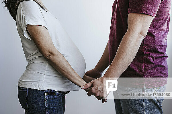 Pregnant woman with man holding hands in front of wall