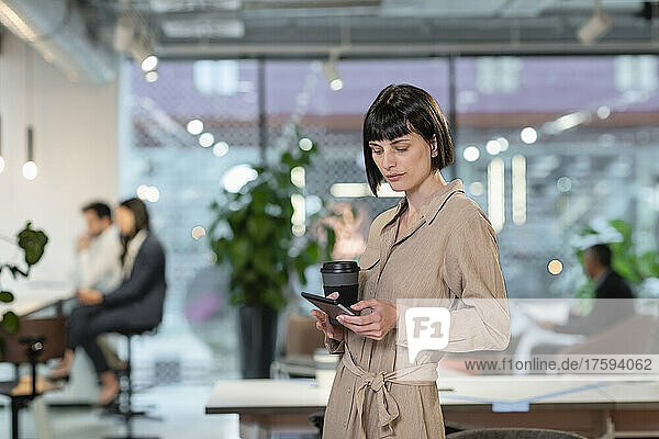 Manager with disposable coffee cup using smart phone in office