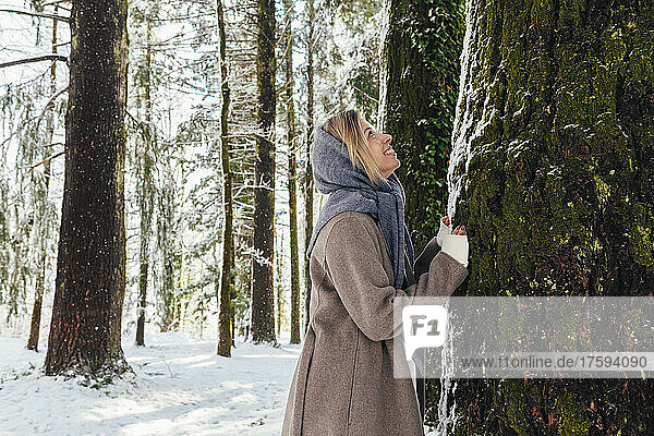 Fröhliche Frau lehnt an Baumstamm im Wald