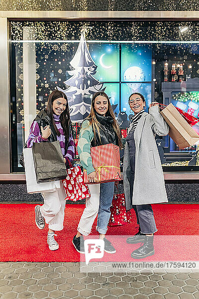 Smiling friends with shopping bags standing on footpath at Christmas