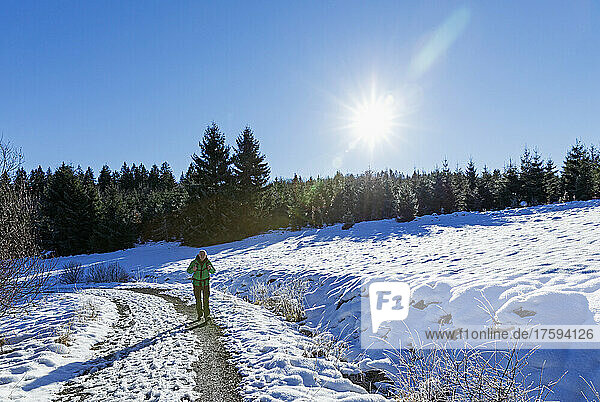 Sun shining over senior hiker walking along snowy road in Perlenbach-Fuhrtsbachtal nature reserve