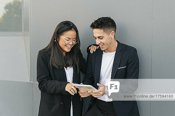 Smiling business colleagues sharing tablet PC in front of gray wall