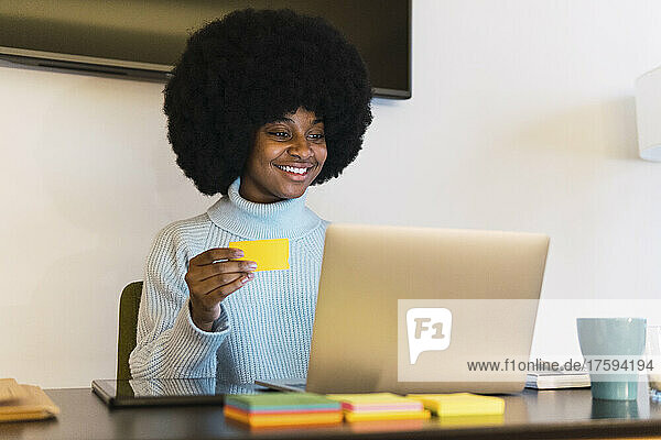 Smiling freelancer with adhesive note looking at laptop at home