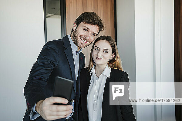 Businessman and businesswoman taking selfie through mobile phone in office