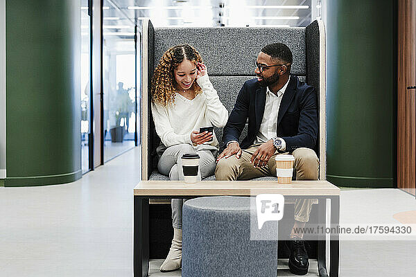 Junger Geschäftsmann spricht in der Kaffeepause im Coworking-Büro mit einem Kollegen per Smartphone