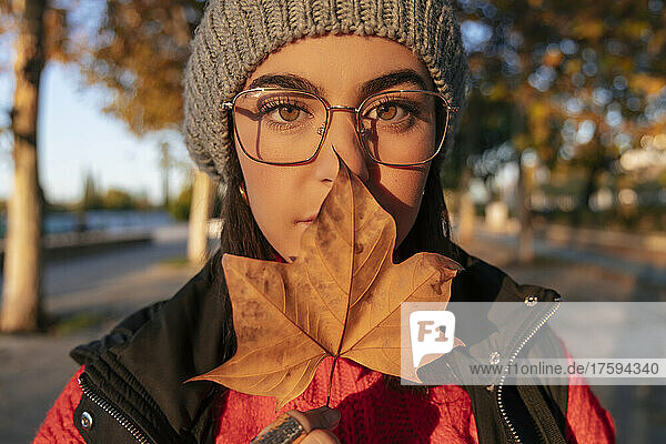 Young woman covering mouth with autumn leaf