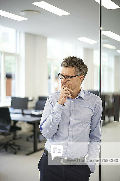 Thoughtful businessman with hand on chin at modern office