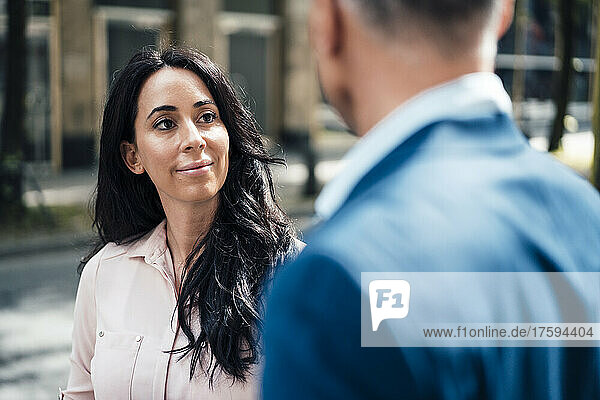 Smiling businesswoman looking at businessman at footpath