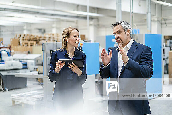 Blond businesswoman with tablet PC looking at colleague discussing in factory