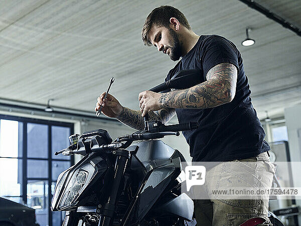Tattooed mechanic with tool working on motorcycle in workshop