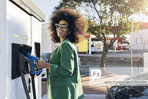 Happy businesswoman with fuel pump at gas station