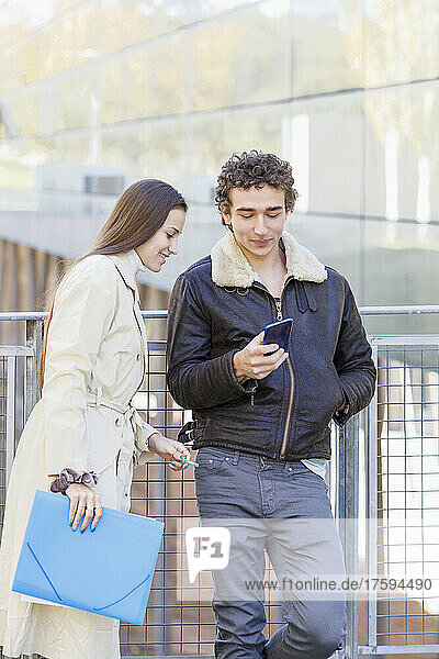 Smiling woman looking at friend using smart phone on campus