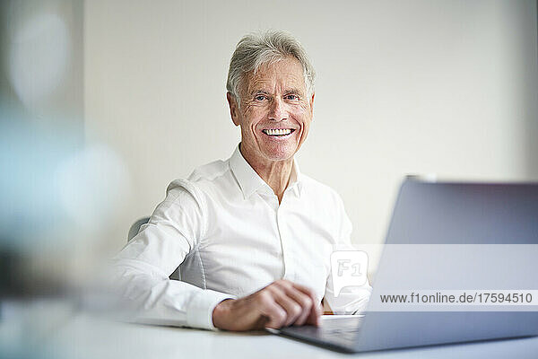 Smiling businessman with laptop at desk in studio