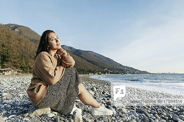 Beautiful young woman sitting on stones at beach