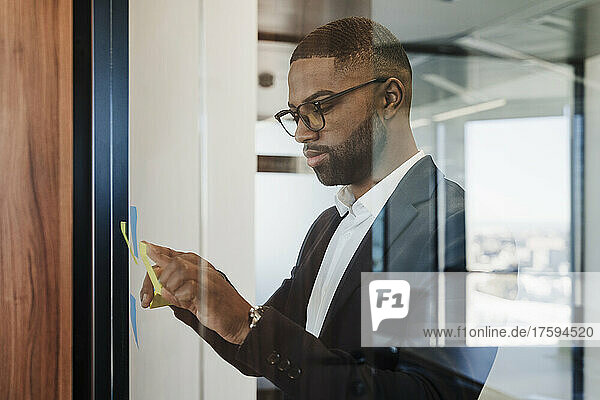 Businessman sticking adhesive note on glass wall at office