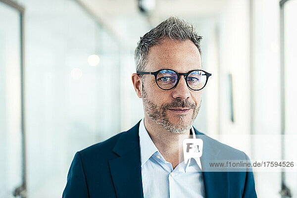 Confident businessman wearing eyeglasses in corridor at office
