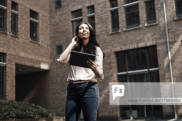 Smiling businesswoman with tablet PC standing in front of building