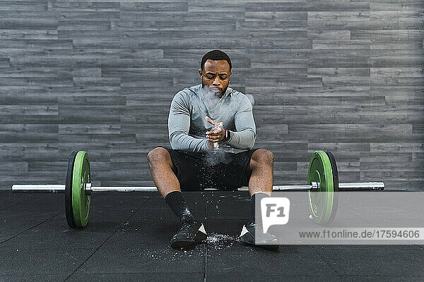 Athlete applying chalk powder sitting on barbell in gym