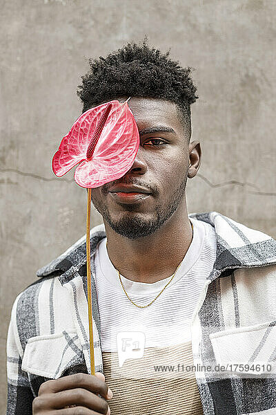 Young man with flamingo lily covering eye in front of wall