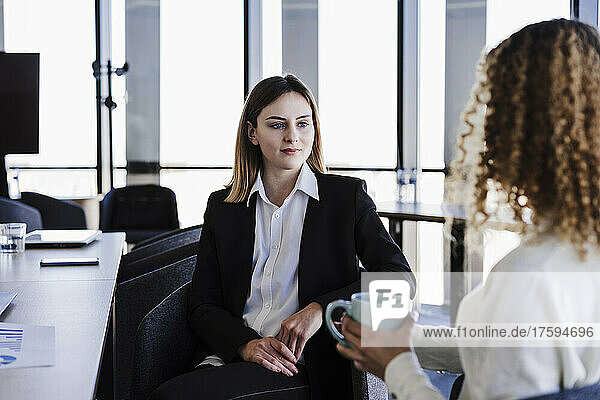 Businesswoman looking at colleague holding mug in coworking office