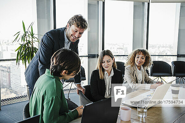 Happy businessman discussing with colleagues sitting at desk in office