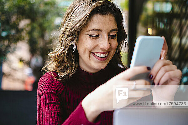 Cheerful woman using mobile phone in sidewalk cafe