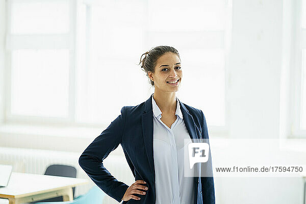 Businesswoman with hand on hip smiling at office