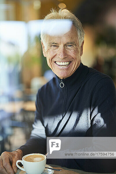 Happy elderly man with coffee cup seen through glass of cafe