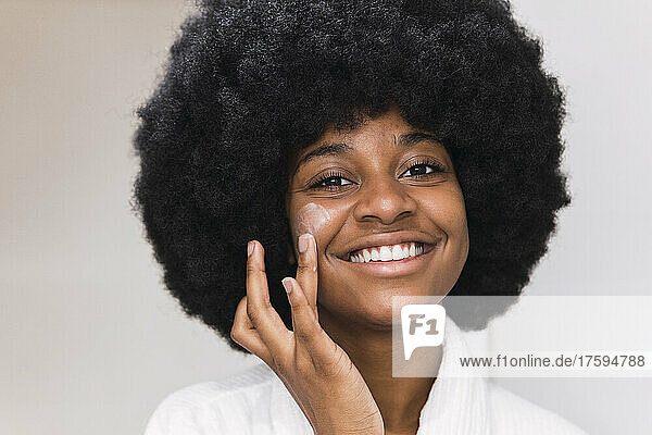 Smiling Afro woman applying face cream