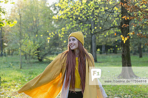 Smiling redhead woman wearing yellow knit hat and scarf day dreaming in autumn park